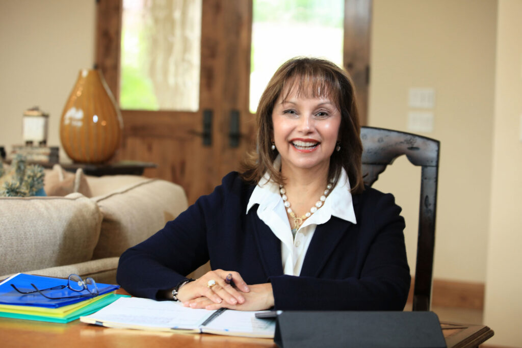 Executive Coach Carmie Saldana sitting at a desk smiling